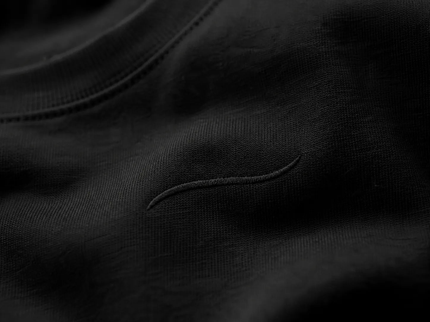 Close-up of the tonal embroidered BRTLS signature mark on the Core Tee Black, highlighting premium craftsmanship and minimalist design.