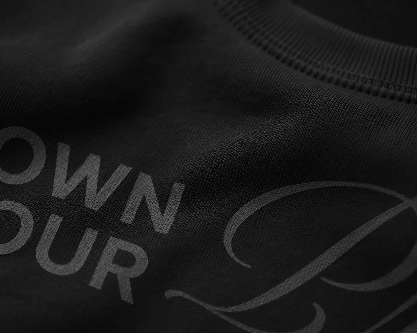 Close-up detail of tonal Own Your Presence artwork printed on heavyweight black premium sweatshirt fabric