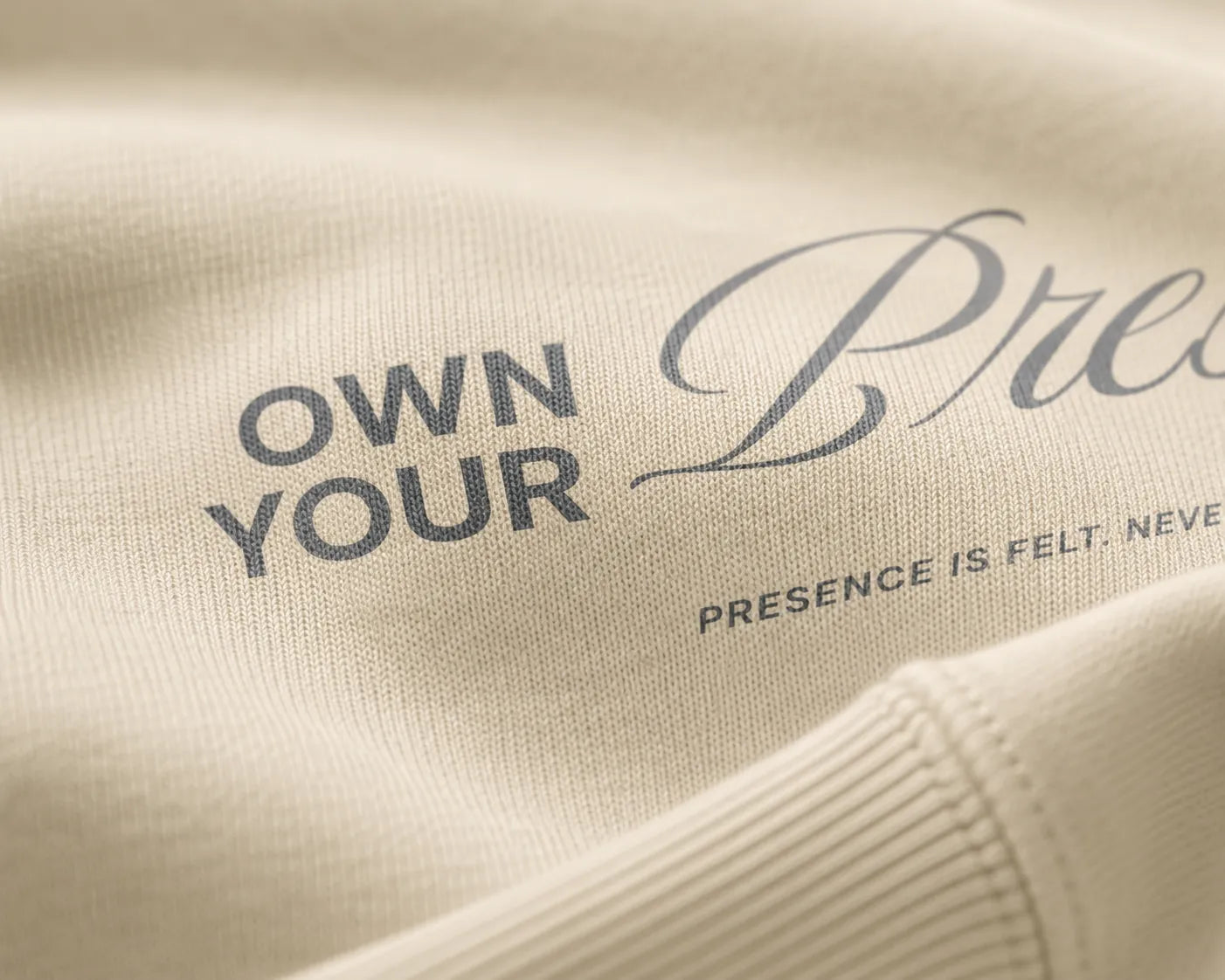 Close-up detail of tonal print and heavyweight cotton fabric on the BRTLS Own Your Presence sweatshirt in bone