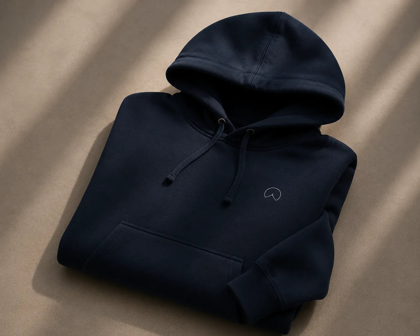 Folded navy BRTLS Presence hoodie with minimalist embroidery and heavyweight premium finish in soft editorial lighting