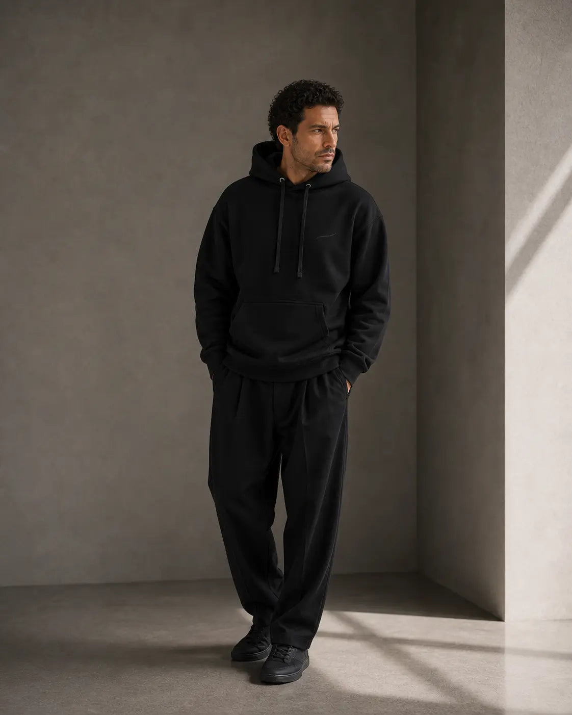 BRTLS Core Hoodie Black worn by model in minimalist interior showcasing premium heavyweight hoodie for modern fatherhood