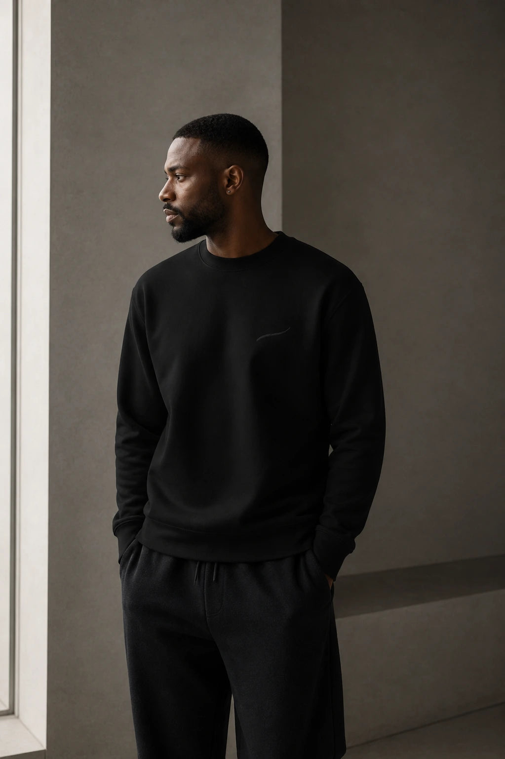 Man wearing the BRTLS Core Sweatshirt Black in a minimalist interior designed for everyday comfort and timeless style