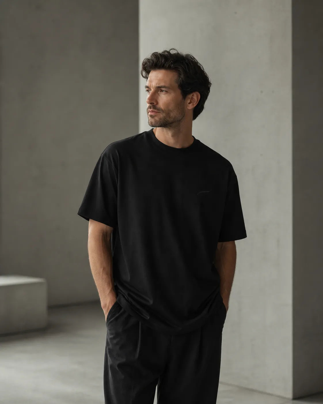 Man wearing the BRTLS Core Tee Black in a minimalist architectural setting, showcasing timeless style and premium heavyweight cotton construction.