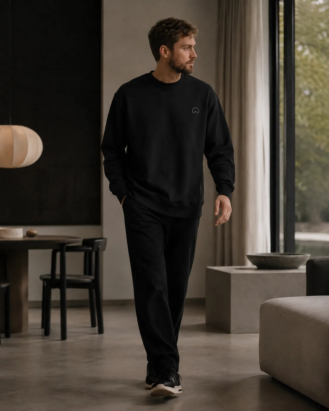 Modern man wearing the black BRTLS Own Your Presence sweatshirt inside a minimalist Scandinavian living space