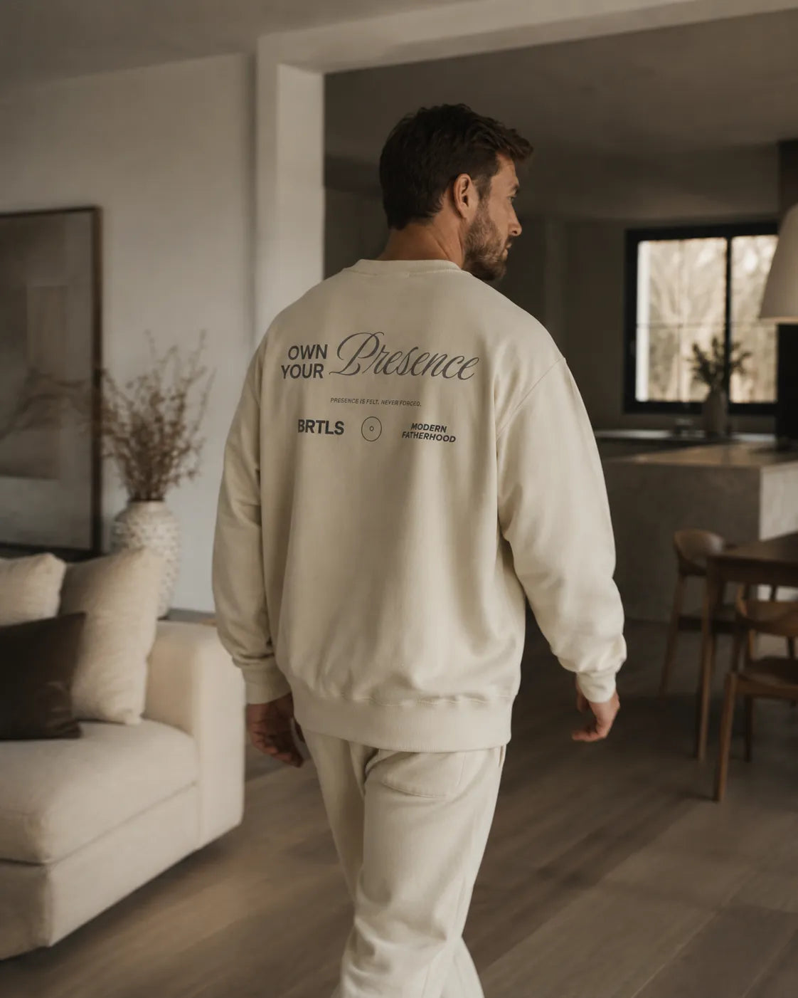 Lifestyle image of a man walking in the BRTLS Own Your Presence sweatshirt in bone