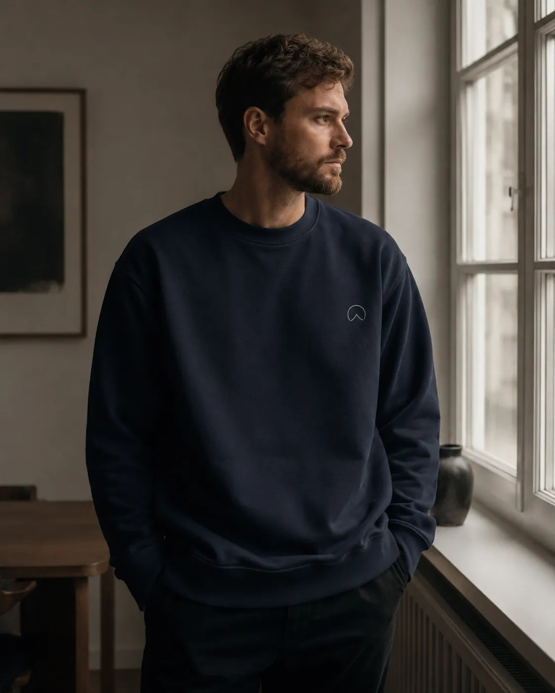 Man wearing BRTLS Own Your Presence Navy Sweatshirt in minimalist interior with refined modern fatherhood styling