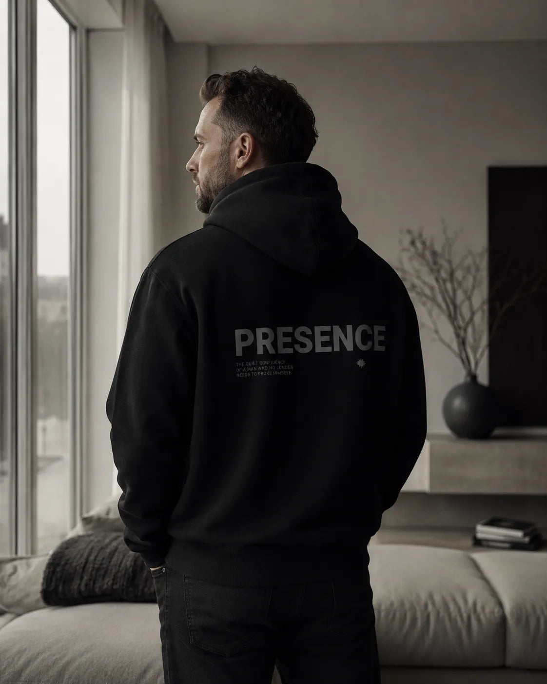 Man wearing The Presence Hoodie Black by BRTLS inside a minimalist Scandinavian interior with cinematic natural light