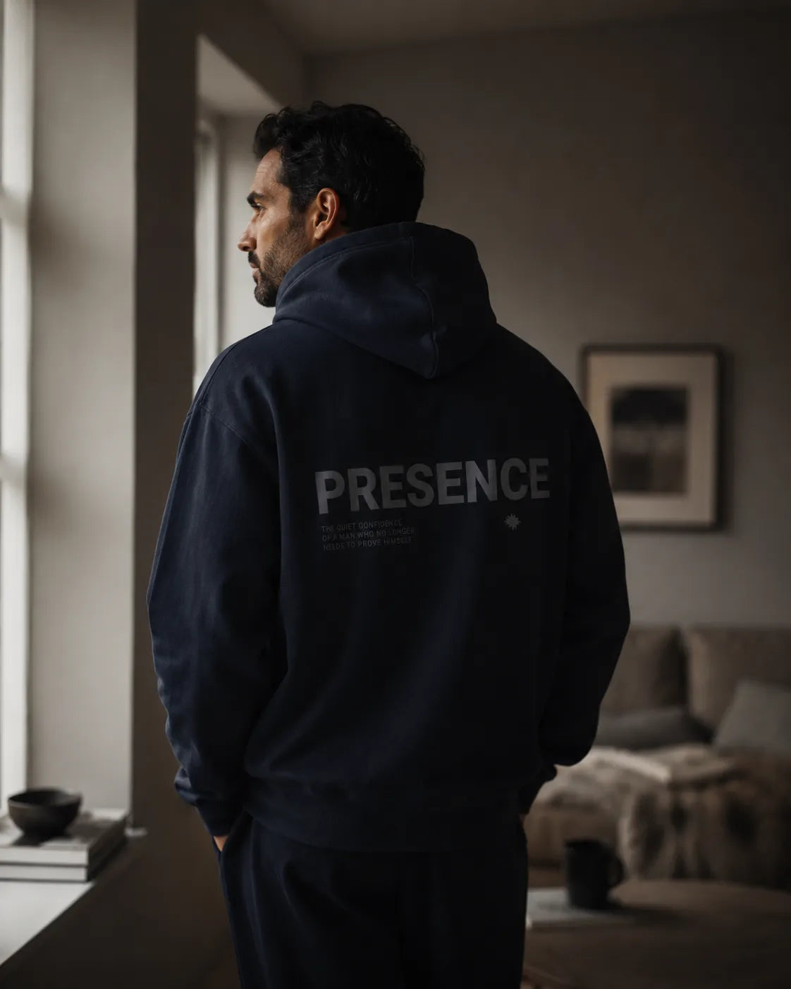Man draagt navy BRTLS Presence hoodie in minimalistisch Scandinavisch interieur met rustige cinematic lifestyle uitstraling
